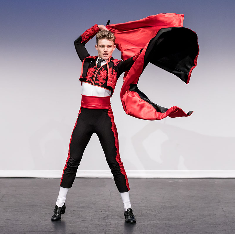 Chase Leathard dances on stage in a matador costume swinging a red cape